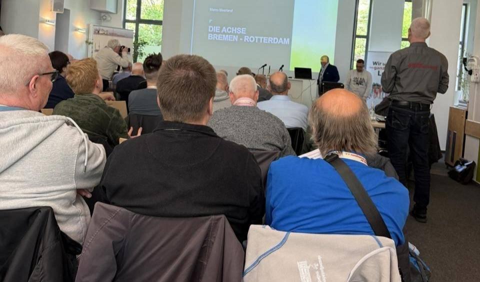 Mehrere Personen sitzen in einem hellen Seminarraum und blicken auf eine Leinwand.